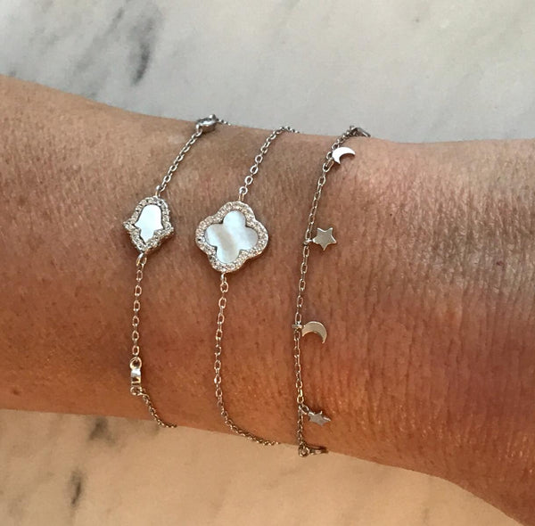 
Sterling silver chain bracelet with a Mother of Pearl clover charm rimmed with cubic zirconia stones, displayed  .

